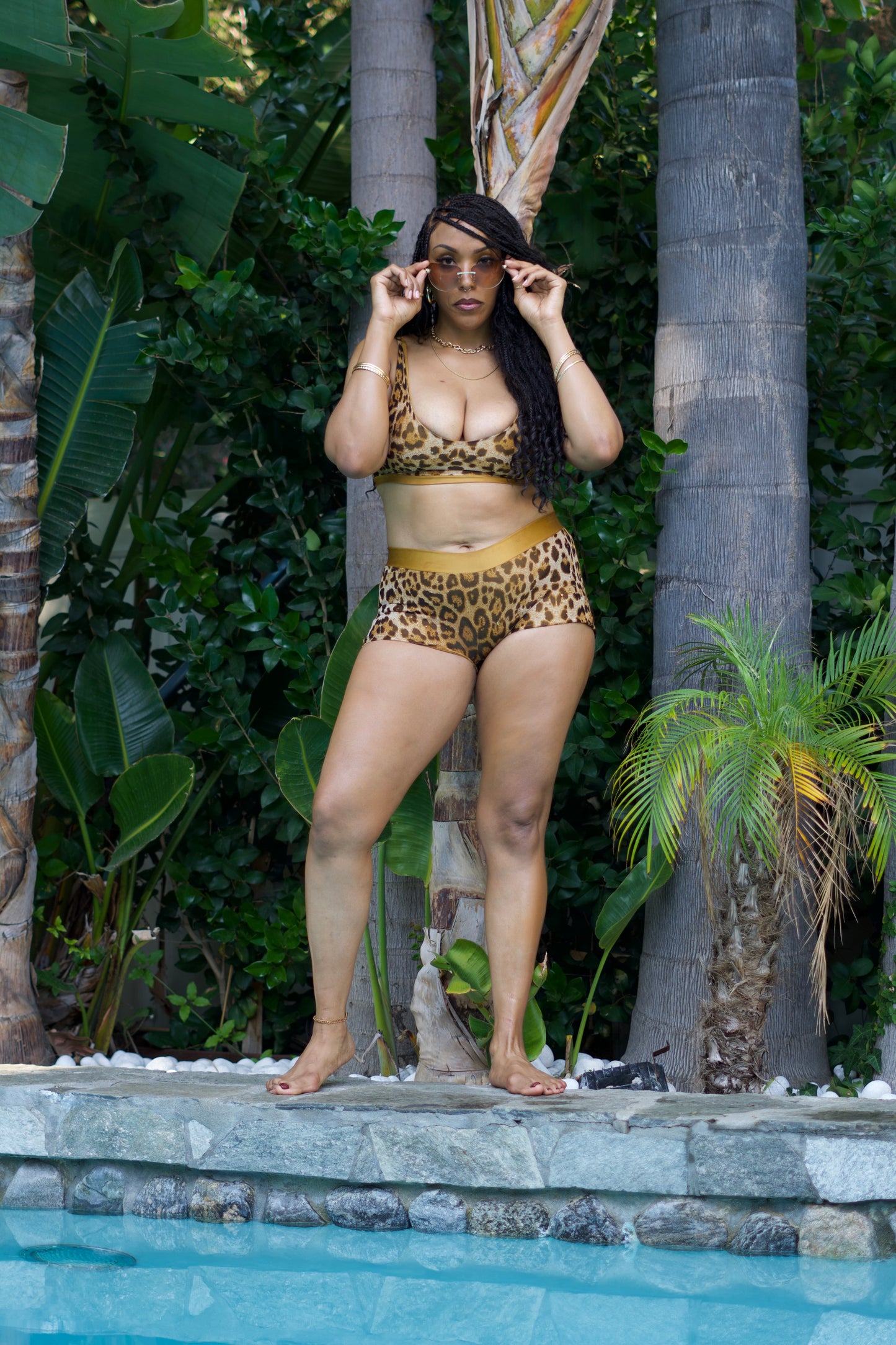 Woman in leopard print bikini standing by a pool with tropical plants in the background