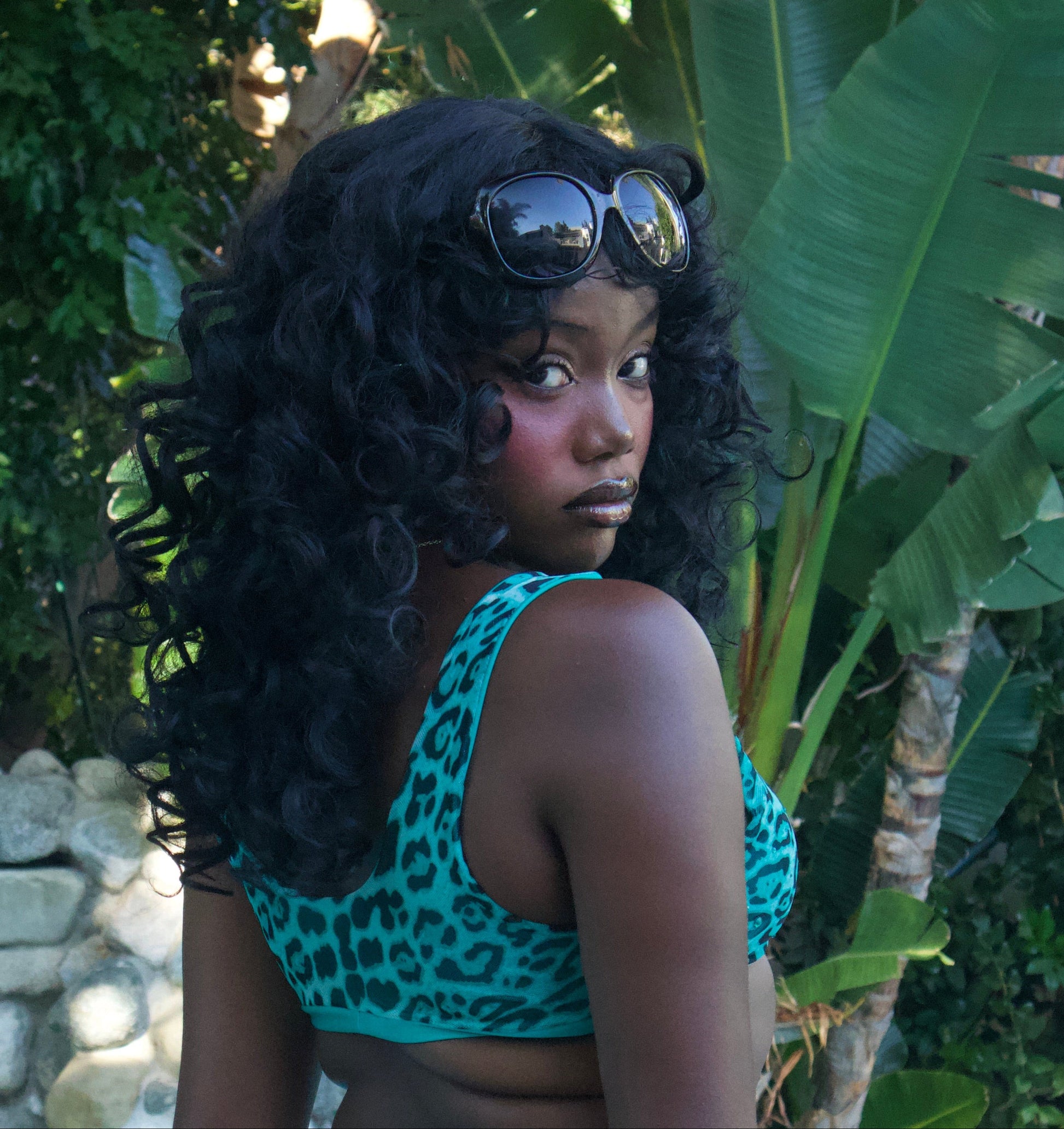 Woman in a turquoise leopard print bikini standing by a pool with greenery in the background